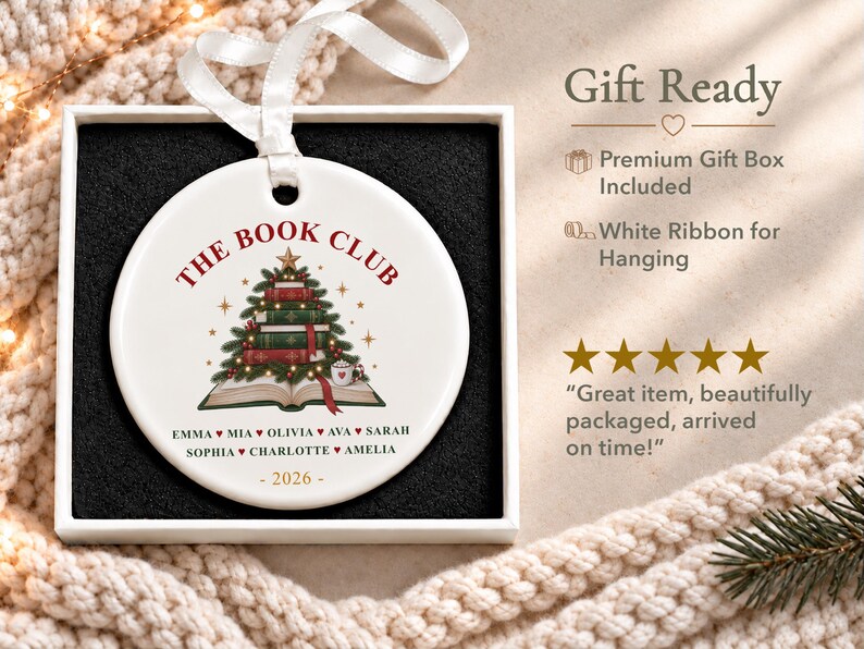 May include: A round white ceramic ornament featuring a graphic of a Christmas tree made of stacked books, with the text THE BOOK CLUB, a list of names including Emma, Mia, Olivia, Ava, Sarah, Sophia, Charlotte, Amelia, and the year 2026, with a white ribbon.