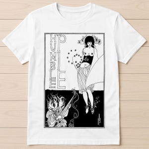 Könnte beinhalten: Weißes T-Shirt mit einer schwarz-weißen Jugendstil-Illustration. Das Design zeigt das Wort "HUMBLE" vertikal, eine Frau und eine Figur, die ein Saiteninstrument spielt. Das Kunstwerk ist in einem schwarzen Rahmen eingefasst.