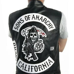 May include: A black leather vest featuring a large embroidered patch on the back. The patch displays a grim reaper holding a rifle and a scythe, with the text SONS OF ANARCHY arched above and CALIFORNIA arched below, plus an MC patch on the side.