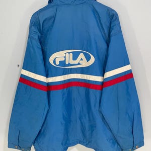 K&ouml;nnte beinhalten: Blaue Fila-Jacke mit wei&szlig;-rotem Streifendesign auf dem R&uuml;cken. Das Fila-Logo ist wei&szlig; dargestellt. Die Jacke hat einen Kragen und Knopfverschl&uuml;sse.