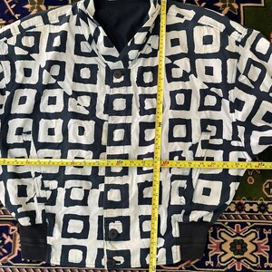 Może przedstawiać: Kurtka w stylu vintage z czarno-białym geometrycznym wzorem. Kurtka ma zapięcie na guziki, czarny kołnierz i czarne prążkowane mankiety. Kurtka ma około 71 cm długości.