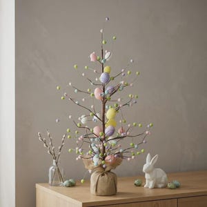 May include: An Easter tree decorated with pastel eggs and green berries on brown branches, set in a burlap-wrapped base. A white ceramic rabbit and decorative eggs are on a wooden surface.