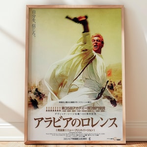 以下が含まれることがあります： 映画「アラビアのロレンス」の額入りポスター。ポスターには、砂漠の背景を背景に、銃を掲げた白いローブを着た男性が描かれています。下部には日本語のテキストがあり、英語で「Lawrence of Arabia」と書かれています。