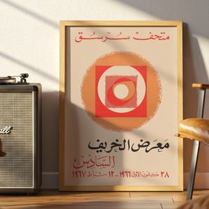 May include: A rectangular framed poster featuring a central graphic of concentric orange and red circles and squares on a cream background. The poster includes Arabic text at the top and bottom, with dates reading 1966 and 1967 at the base.