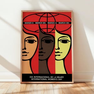 May include: A framed poster featuring a red background with three stylized faces in orange, dark brown, and yellow. Above the faces is a black globe outline. Text reads: MARZO 8 MARCH 8th and DIA INTERNACIONAL DE LA MUJER INTERNATIONAL WOMEN'S DAY.