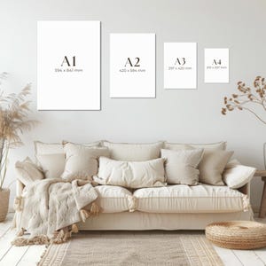 May include: Four white art prints labeled A1 (23.4 x 33.1 inches), A2 (16.5 x 23.4 inches), A3 (11.7 x 16.5 inches), and A4 (8.3 x 11.7 inches) are displayed on a white wall above a beige sofa with pillows and a woven rug.