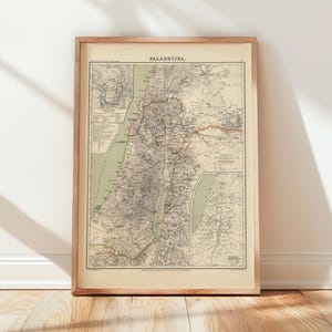 Puede incluir: Mapa antiguo enmarcado de Palestina, con información geográfica detallada. El mapa está en un marco de madera y se apoya contra una pared blanca y un suelo de madera. El título del mapa, "PALESTINA", está impreso en la parte superior.