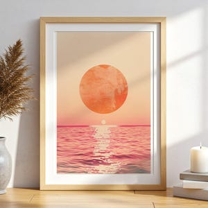 Puede incluir: Una lámina de arte enmarcada que muestra un sol grande y texturizado de color naranja sobre una superficie oceánica tranquila y ondulada al atardecer. La obra presenta un degradado de tonos melocotón y rosa cálidos que reflejan la luz.