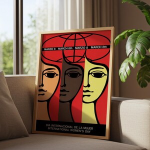 May include: A framed poster featuring a graphic illustration of three stylized faces in orange, brown, and yellow against a red background. The text reads MARZO 8, MARCH 8th, and DIA INTERNACIONAL DE LA MUJER INTERNATIONAL WOMEN'S DAY.