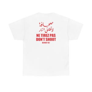 Peut inclure: T-shirt blanc avec texte rouge et caractères arabes. Le texte comprend "NE TIREZ PAS DON'T SHOOT" et "BEIRUT 82". Un vêtement décontracté.
