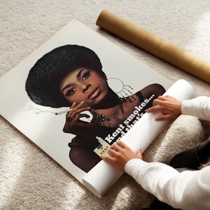 May include: A vintage poster featuring a woman with a large afro smoking a cigarette. The poster has the text "Kent smokes... and that's". The poster is rolled up with a brown tube.