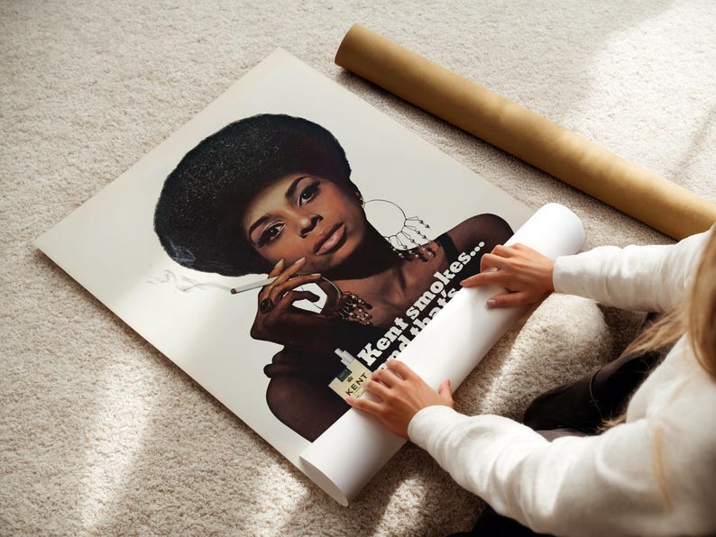 May include: A vintage poster featuring a woman with a large afro smoking a cigarette. The poster has the text "Kent smokes... and that's". The poster is rolled up with a brown tube.