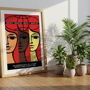 May include: A framed poster featuring a graphic illustration of three stylized faces in shades of tan, brown, and yellow against a red background. The text reads "MARZO 8", "MARCH 8th", and "DIA INTERNACIONAL DE LA MUJER INTERNATIONAL WOMEN'S DAY".