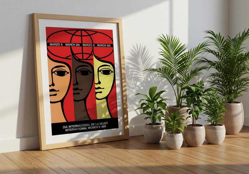 May include: A framed poster featuring a graphic illustration of three stylized faces in shades of tan, brown, and yellow against a red background. The text reads "MARZO 8", "MARCH 8th", and "DIA INTERNACIONAL DE LA MUJER INTERNATIONAL WOMEN'S DAY".
