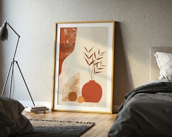 Puede incluir: Una impresión artística enmarcada con un diseño abstracto. Presenta un jarrón de terracota con ramas frondosas. La obra de arte tiene un marco dorado e incluye formas geométricas en tonos naranja, beige y marrón. La impresión está apoyada contra una pared.