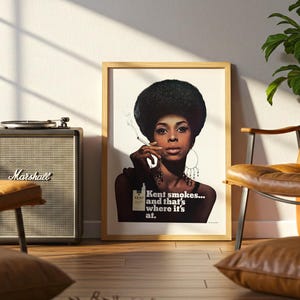 May include: A framed vintage poster featuring a woman with a large afro smoking a cigarette. The poster has the text "Kent smokes... and that's where it's at." A Marshall speaker and a record player are next to the poster. A leather chair and a plant are also in the room.