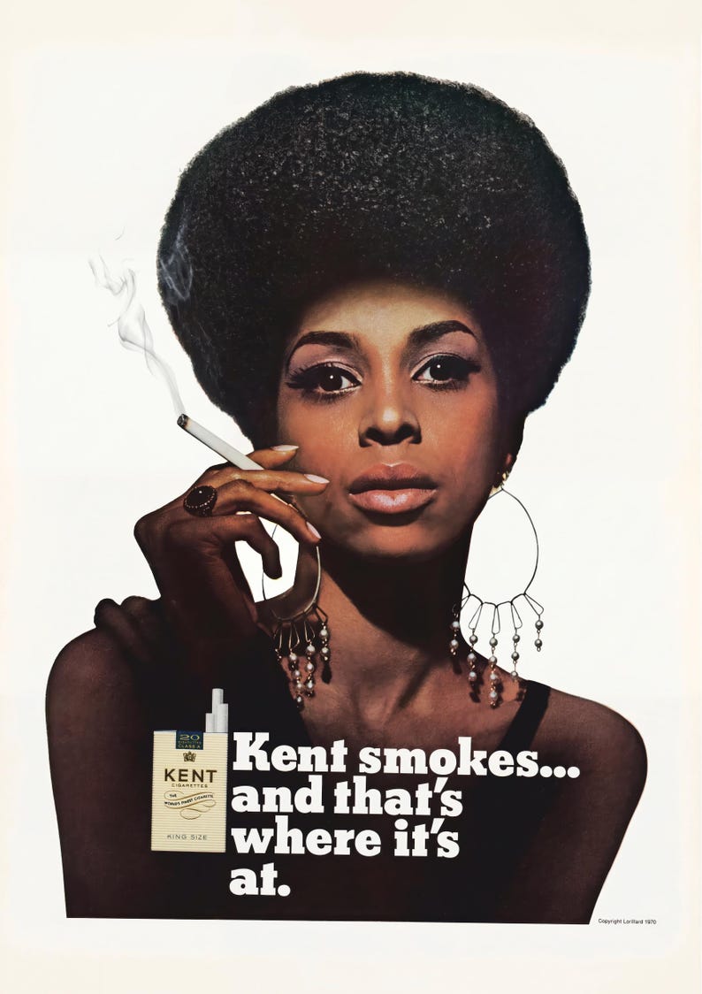 May include: Vintage advertisement featuring a woman with a large afro, wearing large hoop earrings, and smoking a cigarette. The ad includes a pack of Kent cigarettes and the text "Kent smokes... and that's where it's at."