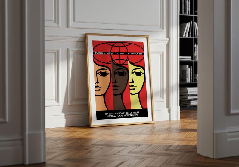 May include: A framed poster featuring a stylized graphic illustration of three faces in tan, brown, and yellow against a red background. Above the faces is a globe outline and the text "MARZO 8 MARCH 8th". Below is "DIA INTERNACIONAL DE LA MUJER INTERNATIONAL WOMEN'S DAY".