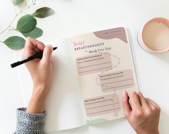 May include: A pink and white journal with the title "Belief Breakthroughs" and the text "Break Free Map". The journal has three sections: "Limiting Belief I'm working on", "Where it shows up in my life", and "What freedom looks like".