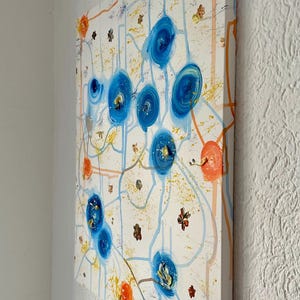 Könnte beinhalten: Abstraktes Gemälde auf Leinwand mit weißem Hintergrund. Das Kunstwerk zeigt blaue Kreisformen, orange und gelbe Akzente sowie dünne blaue und orangefarbene Linien. Kleine braune Blumenformen sind im gesamten Design verstreut.