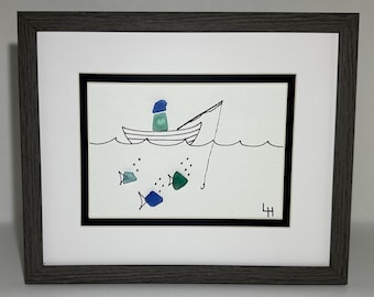 May include: Framed artwork depicting a fishing scene. A small boat with a figure in a blue hat is on the water, fishing with a line. Three colorful fish are in the water. The artwork is framed in a gray wooden frame.