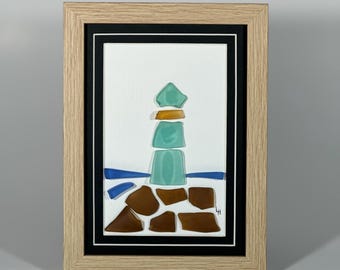 Könnte beinhalten: Ein gerahmtes Kunstwerk, das einen Leuchtturm aus Meerglas darstellt. Der Leuchtturm ist grün, braun und orange. Das Meerglas ist in einem Mosaikmuster angeordnet. Das Kunstwerk ist vor einem weißen Hintergrund platziert.