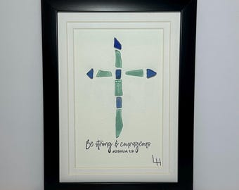 Könnte beinhalten: Gerahmtes Kunstwerk mit einem Kreuzdesign aus blauen und grünen Glasstücken. Das Kreuz befindet sich auf einem weißen Hintergrund, darunter die Worte "Be strong & courageous" und "Joshua 1:9". Der Rahmen ist schwarz.