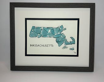 May include: Framed artwork featuring a map of Massachusetts, constructed from turquoise glass pieces. The state's name is printed in black below the map. The artwork is set against a white background, framed in a dark gray wooden frame.