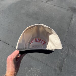 May include: A cream-colored baseball cap with a black brim and a plastic snapback closure. The interior back panel features the red embroidered text "LAFITTE" in a bold, arched font, positioned directly above the adjustable snapback strap.