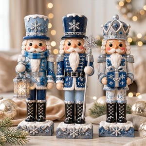 May include: Three decorative nutcracker figurines in shades of blue, white, and silver. The left figure holds a lantern, the centre figure holds a snowflake staff, and the right figure holds a gift box. All wear tall hats with snowflake motifs.