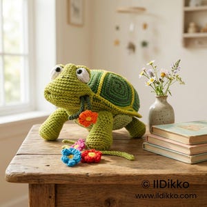 May include: A green crocheted turtle toy with large white eyes, featuring a dark green shell with a spiral pattern. The turtle holds a small orange crocheted flower in its mouth, with additional blue, red, and pink crocheted flowers nearby.