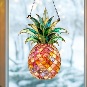 May include: A stained glass pineapple suncatcher featuring a textured, multi-faceted body in shades of pink, orange, and yellow. The top consists of pointed, vibrant green and teal glass leaves. The piece hangs from a black metal chain.