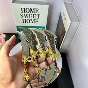 May include: Four decorative miniature swords with ornate gold and red handles, silver blades, and attached chains. The blades have a detailed floral design. The swords are held in a hand, with a book that says "HOME SWEET HOME" in the background.