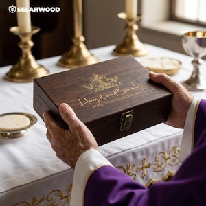 May include: A rectangular dark brown wooden keepsake box with a gold metal latch. The lid features a gold engraved design of a cross and cherubs, with the text Hayden Brooks and BAPTIZED SEPTEMBER 26, 2026, centered on the top surface.