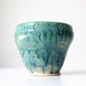 May include: A ceramic bowl featuring a variegated glaze in shades of teal, turquoise, and deep blue. The surface displays a distinct drip pattern where the darker blue glaze runs vertically over a lighter, textured base, ending at a plain rim.