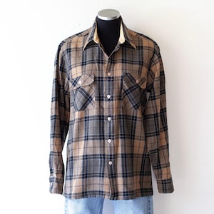 May include: A long-sleeved plaid shirt in shades of brown, navy, and gray, displayed on a mannequin. The shirt features two chest pockets and a button-down front. The collar has a contrasting tan lining.