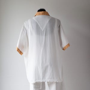 May include: White short-sleeved shirt with a tan collar and sleeve trim. The shirt is made of a lightweight fabric and has a relaxed fit. The shirt is displayed on a mannequin.