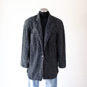 May include: A dark gray blazer with a textured weave, single-button closure, and three buttons on each sleeve. The blazer is displayed on a mannequin, paired with a black top and blue jeans.