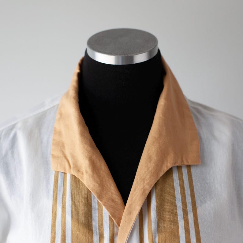 May include: White shirt with a tan collar and vertical stripes in tan and white. The shirt is displayed on a black mannequin, showcasing the collar and front panel design. The shirt's design is a classic retro style.