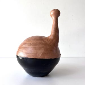 May include: A ceramic vase with a rounded body and a long, thin neck. The vase is painted in two colors: brown on the top and black on the bottom.