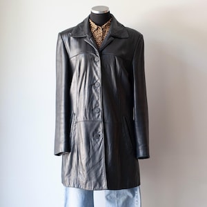 May include: A black leather coat with a collared neckline and button-down closure. The coat is displayed on a mannequin, revealing a leopard print shirt underneath. The coat has a classic, tailored design.