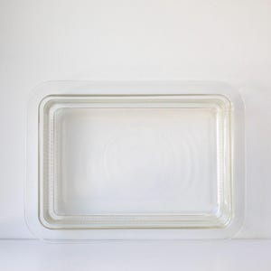 May include: A clear, rectangular glass baking dish with rounded corners. The dish has a layered design, with a slightly textured interior and a smooth, transparent exterior. The overall shape is a simple, functional design.