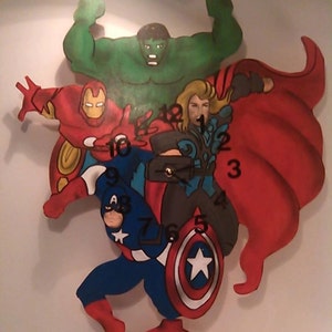 May include: A clock featuring a red, green, and blue superhero theme. The clock face is surrounded by the Avengers logo and features the numbers 1 through 12. The clock hands are black and silver.