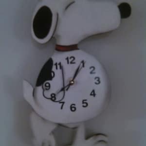 May include: White and black Snoopy wall clock with a round clock face and black numbers. The clock hands are black and the clock face is white. The clock is shaped like Snoopy standing on two legs.