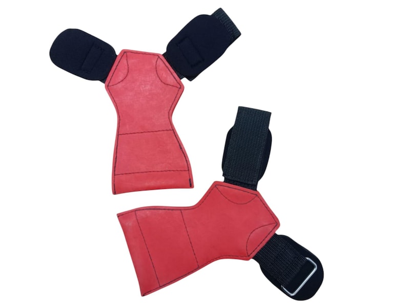 May include: Two red weightlifting grips with black wrist straps. The grips are made of a textured material and have a unique shape. The wrist straps have a hook and loop closure.
