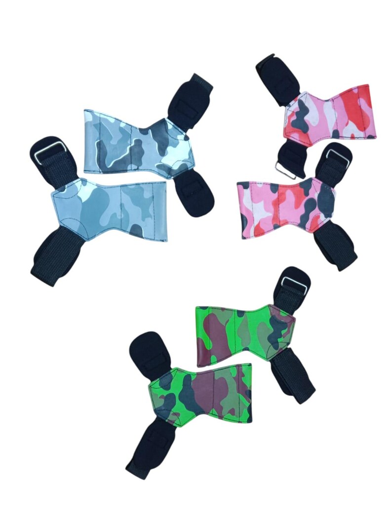 May include: Five weightlifting wrist wraps in various camouflage patterns. The wraps feature black wrist straps and buckles. The camouflage patterns include shades of blue, pink, red, and green.