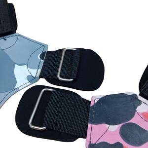 May include: Two weightlifting wrist straps. One strap features a gray camouflage pattern, and the other has a pink and red camouflage pattern. Both straps have black fabric and metal buckles.