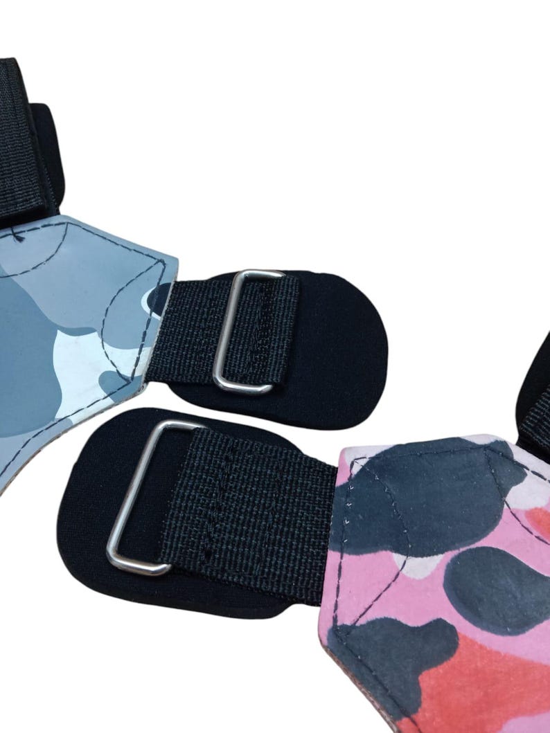 May include: Two weightlifting wrist straps. One strap features a gray camouflage pattern, and the other has a pink and red camouflage pattern. Both straps have black fabric and metal buckles.