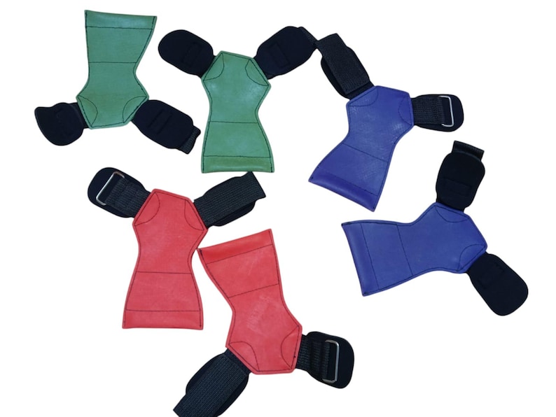 May include: Assortment of weightlifting grip pads in green, red, and blue. Each pad has a contoured shape with a black wrist strap and a hook-and-loop closure for secure grip during workouts. The pads are designed to protect hands and improve grip.