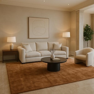 Puede incluir: Salón con sofá y sillón beige, mesa de centro redonda y alfombra marrón. Dos lámparas y arte abstracto completan la decoración. La habitación tiene una paleta de colores neutros.